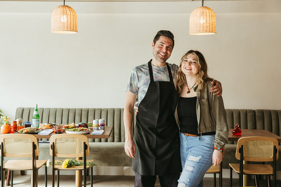 Chef Tolga and his wife Ada are standing in Lokanta Mediterranean Café with tables and chairs in the background